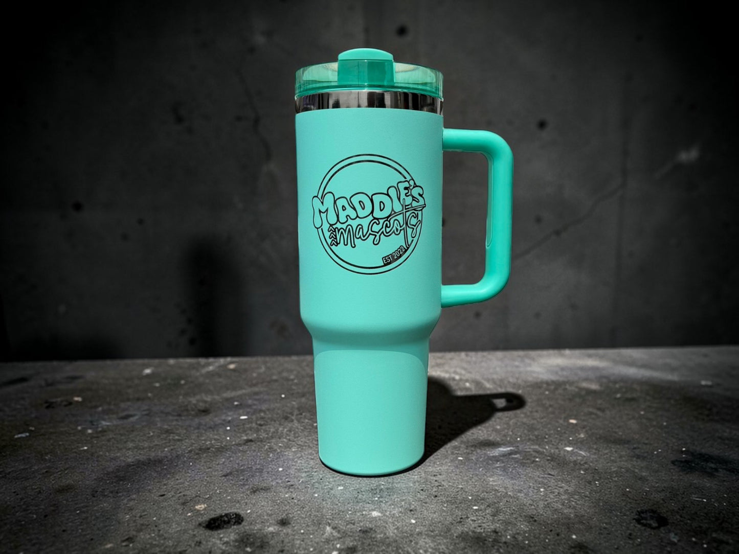 Turquoise travel mug with a handle on a dark surface